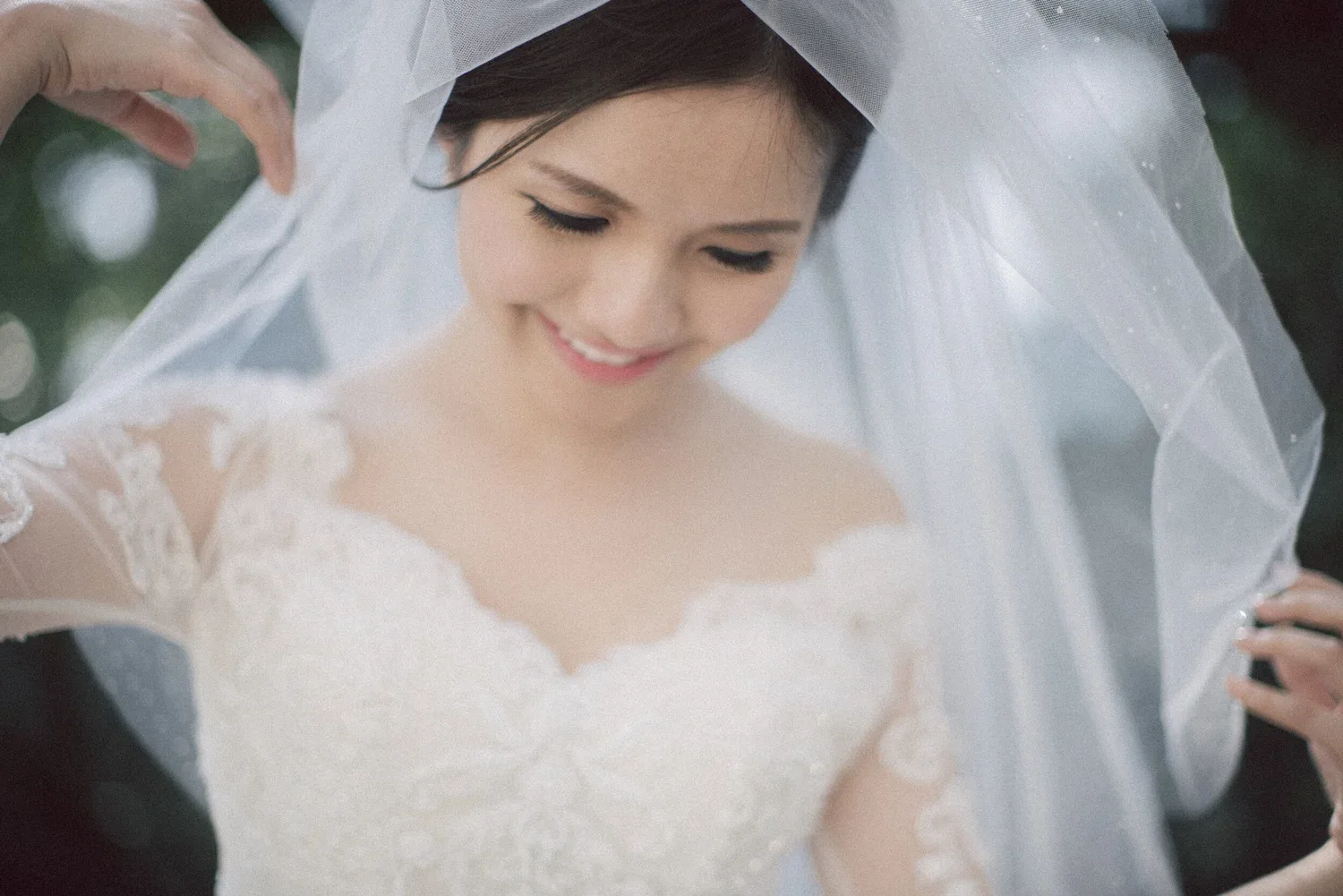 蕾絲婚紗新娘低頭微笑,身旁的手替她整理頭紗