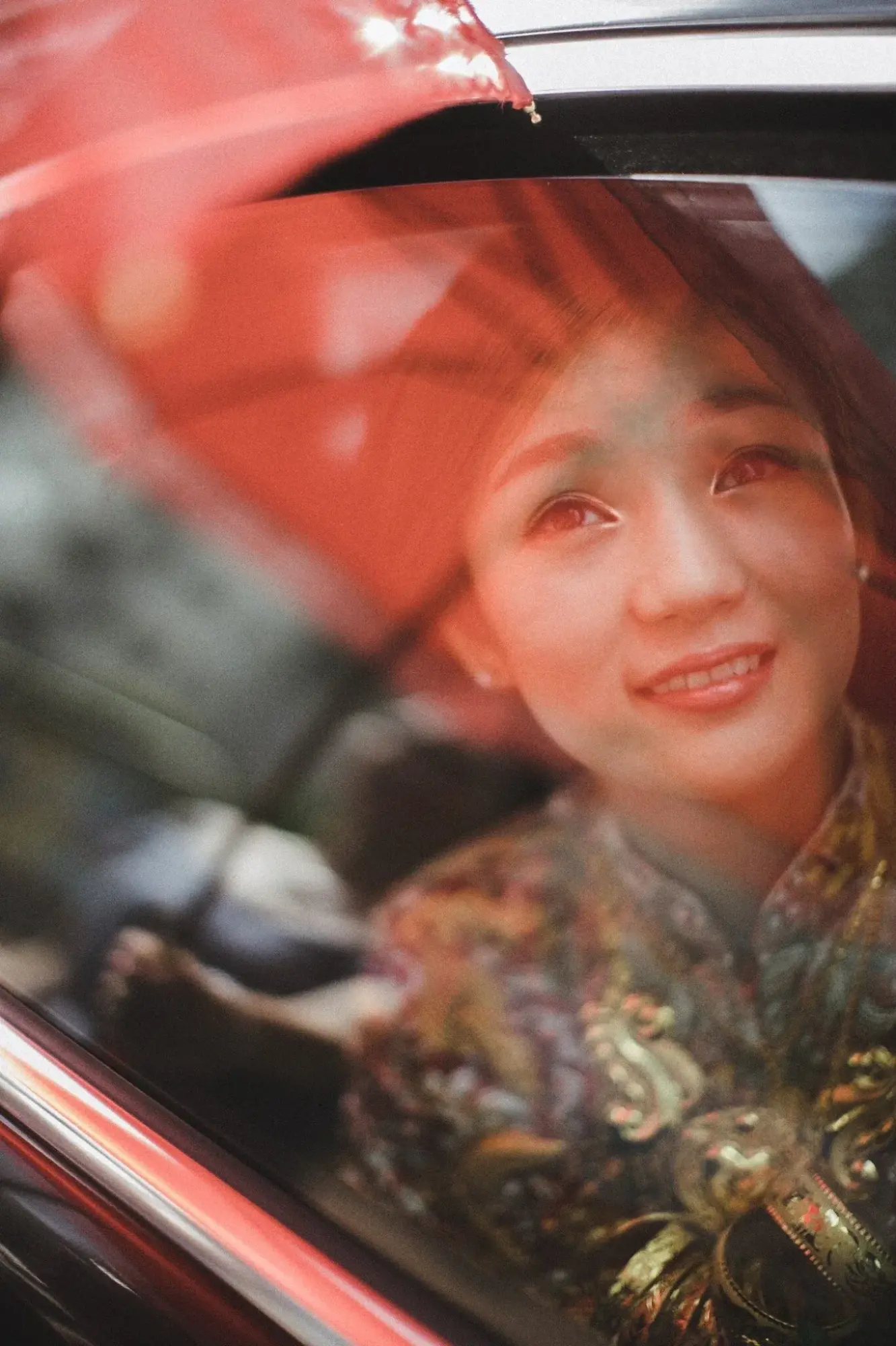 穿裙褂的新娘坐在車內微笑,車窗映着紅色光影