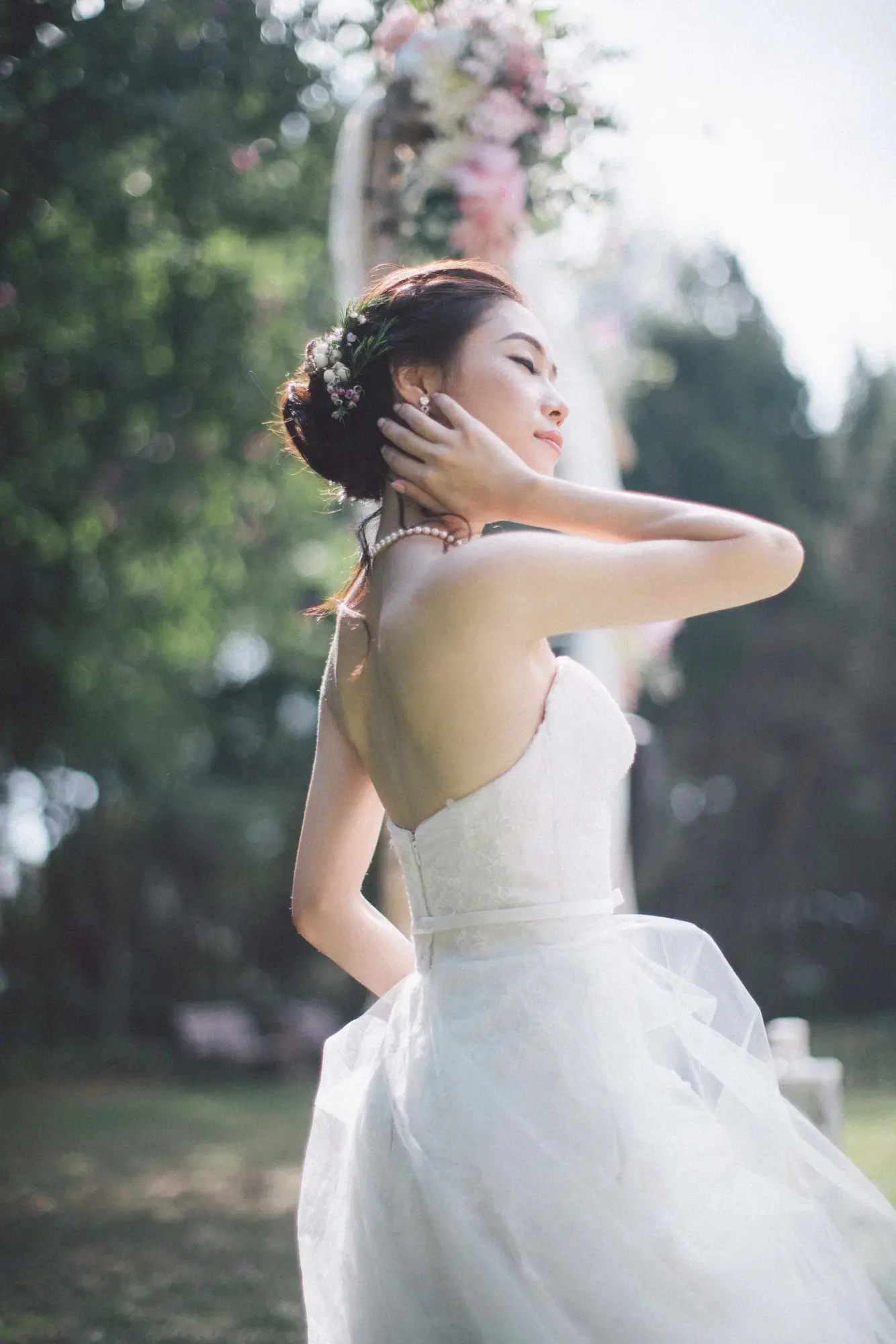 露背婚紗新娘在戶外側身,抬手輕觸後頸