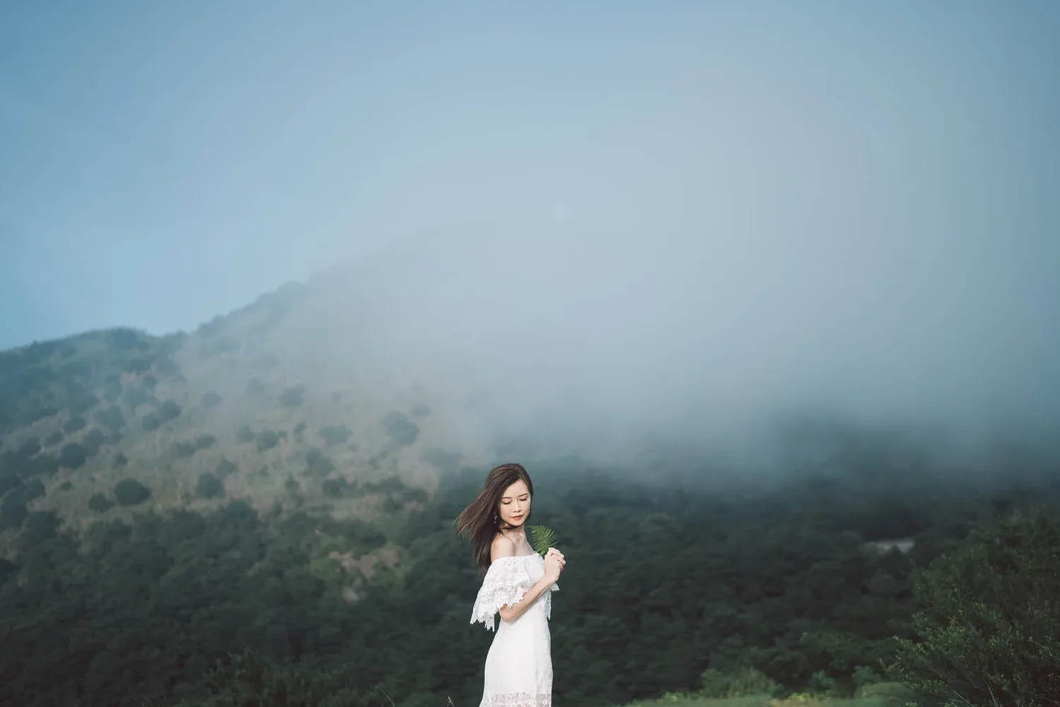 新娘抱着花球站在山坡前,身後山嶺被薄霧包圍