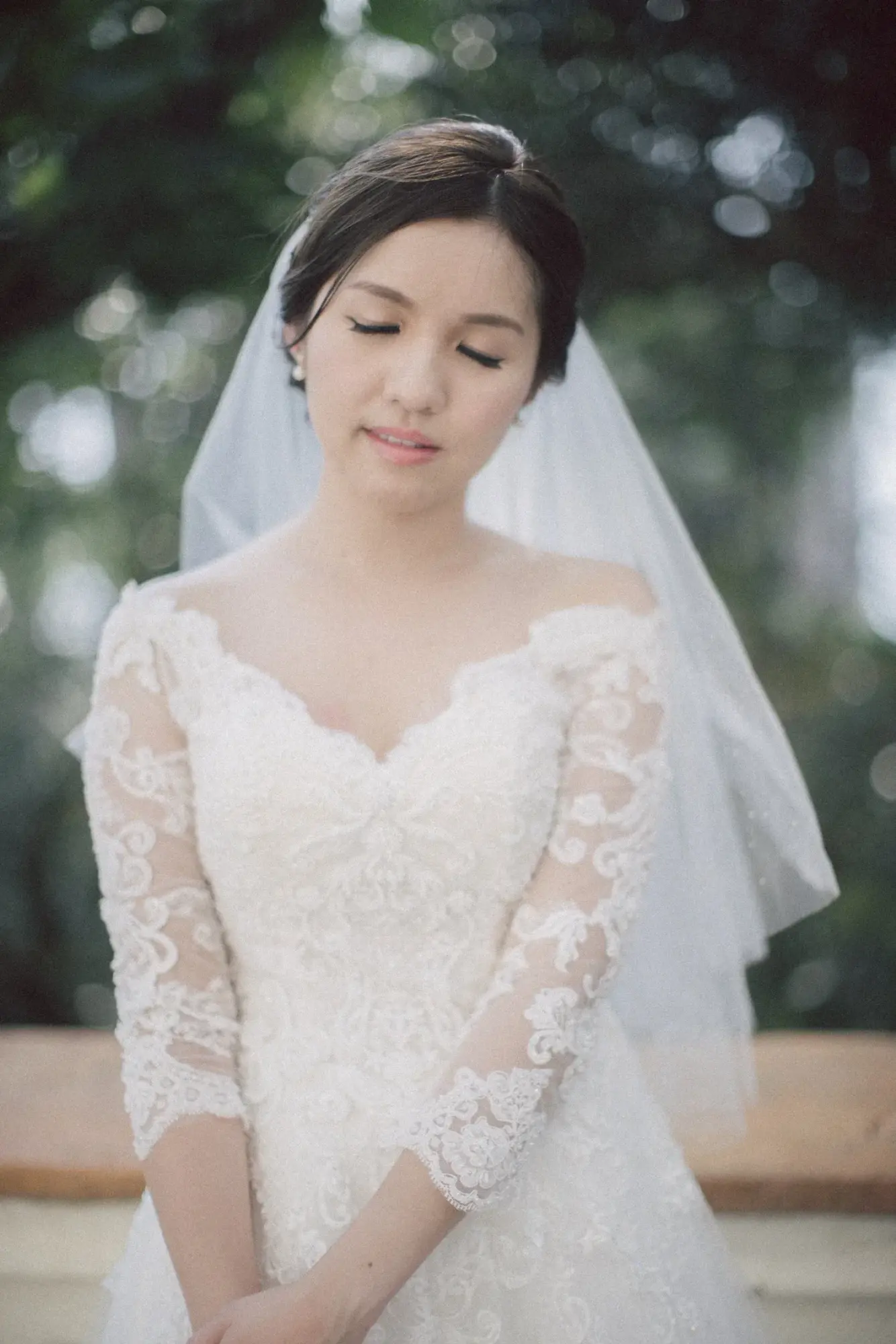 長袖蕾絲婚紗新娘在綠葉前低頭閉眼
