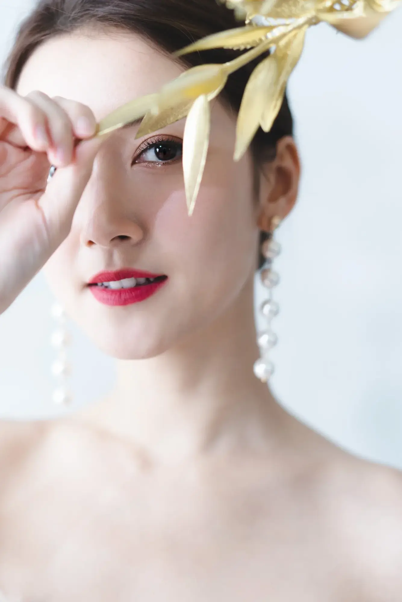 新娘抬手碰觸垂下的金色葉飾,紅唇與長耳飾清晰可見