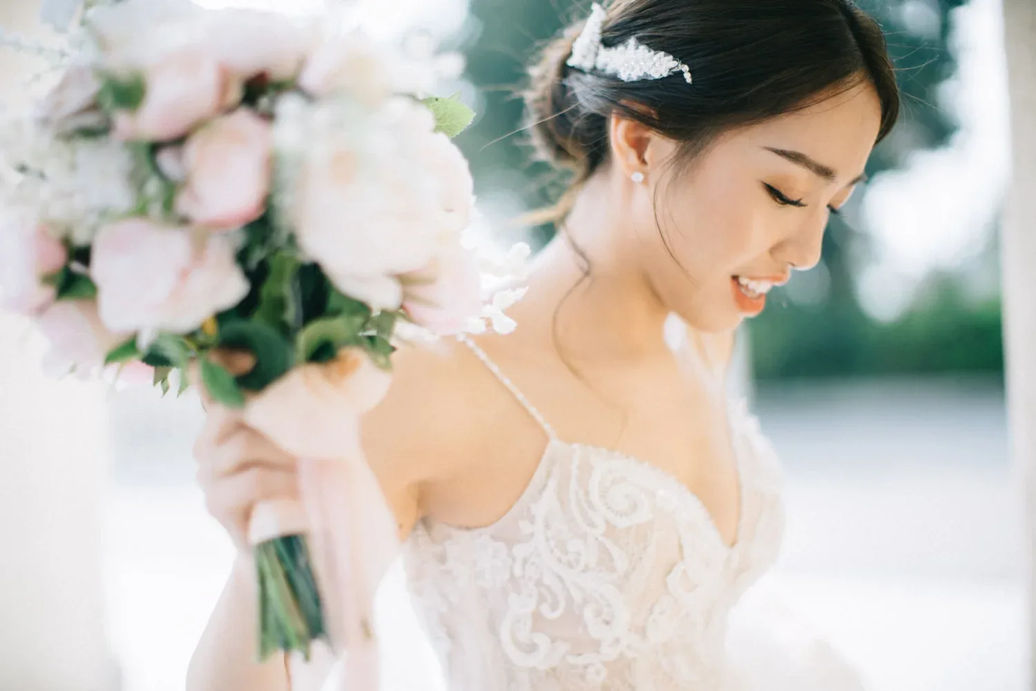 白色蕾絲婚紗新娘低頭微笑,身旁是粉白花藝