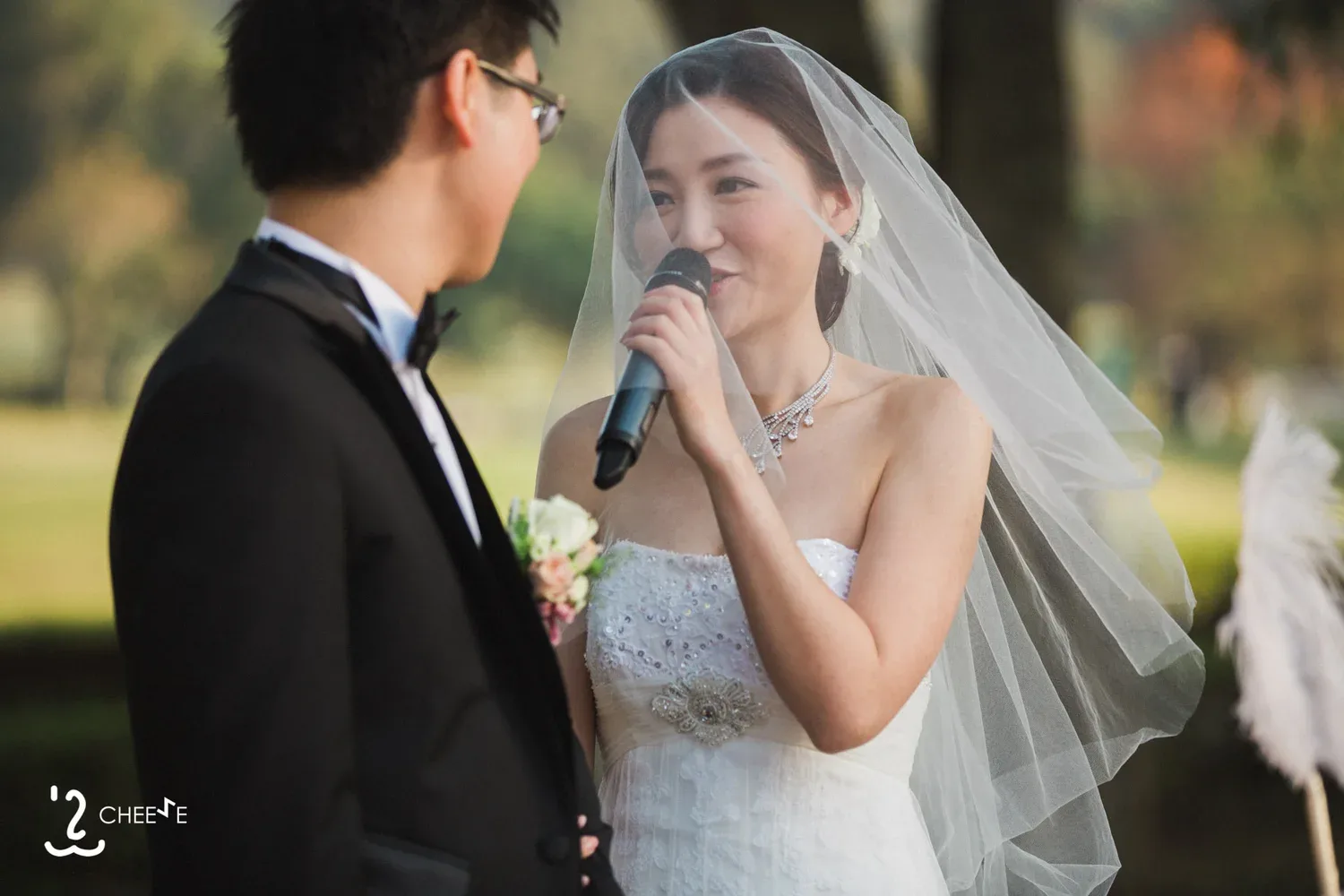 新娘在戶外手持咪高峰向新郎說話,頭紗垂在肩後